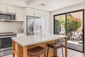 A modern kitchen with stainless steel appliances, a built-in water dispenser, and a large island with stools. - *Palm Valley CC, 76643 Daffodil Dr (Palm Desert)