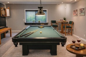 A pool table with cues, a dartboard, and a window with blinds.