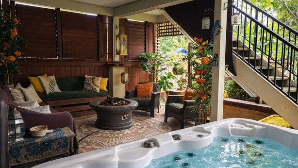 Ein Whirlpool mit Feuerstelle, einer Couch und Korbsesseln in einer überdachten Außenbereich mit Holzterrasse und Treppe.
