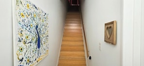 A hallway with a wooden staircase, a large abstract painting on the left, and a heart-shaped picture on the right.
