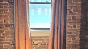 Ein Zimmer mit einem großen Fenster, braunen Vorhängen, einer Ziegelwand und einem Holzboden.
