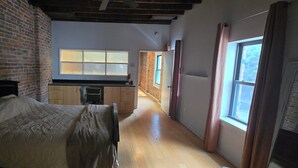 Ein Schlafzimmer mit Bett, Backsteinwand, Fenster und einer Küchenzeile mit Schränken und Arbeitsplatte.