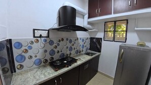 A kitchen with a gas stove, a hood, a refrigerator, and a window with a view. - Thulasi My Village My Resort (Papireddipatti)