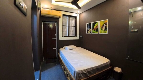 A small, compact bedroom with a single bed, a door, and a window.