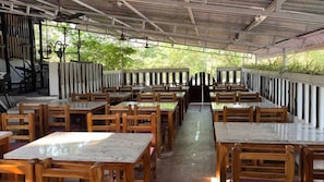Un comedor interior con mesas y sillas de madera, un ventilador de techo y vistas al exterior con follaje.
