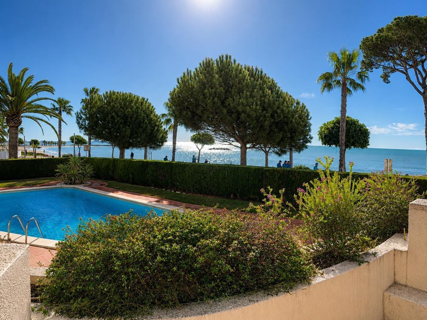 A swimming pool with a view of the sea, surrounded by trees and a clear sky.