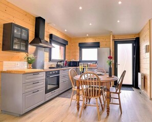 A modern kitchen with grey cabinets, a stainless steel range, and a wooden dining table with chairs. - Le Chalet de la Baie (PLEINE FOUGERES)