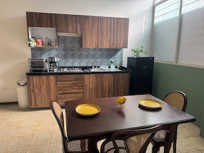 A compact kitchen with wooden cabinets, a herringbone backsplash, a black refrigerator, and a dining table with yellow plates.