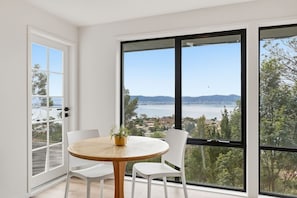 Ein Balkon mit Tisch und Stühlen, einem Blumentopf und Blick auf ein Gewässer sowie die entfernte Landschaft.