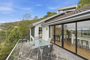 Ein modernes Haus mit einer Glas-Essbereich, einer Holzterrasse und Blick auf die umliegende Landschaft.