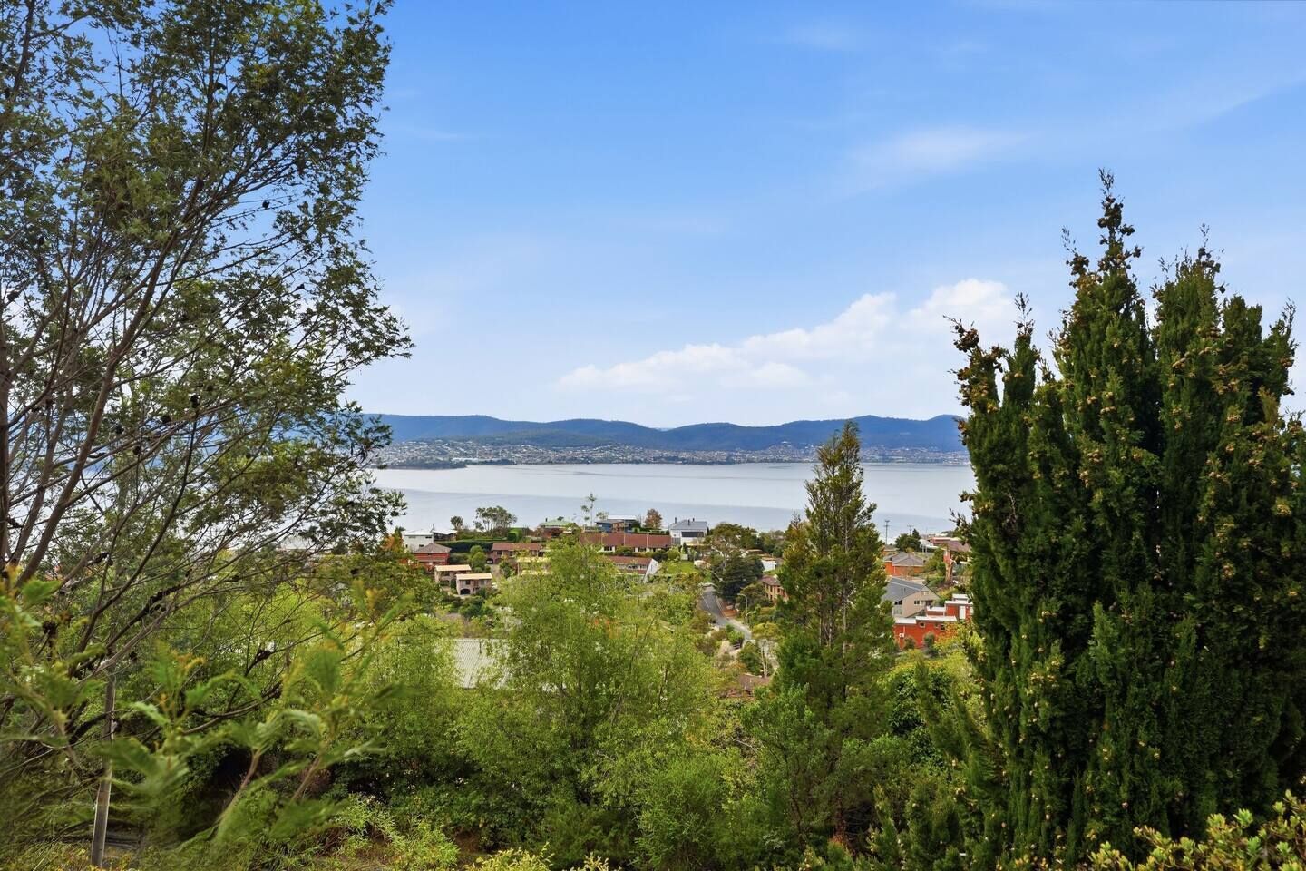 Un pueblo costero con edificios residenciales, vista al mar y montañas a lo lejos.