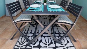 A dining area with a table set for four, a ceiling fan, a sliding glass door, and a small kitchen area with a refrigerator. - LARIMAR APARTMENT (Saint Martin)