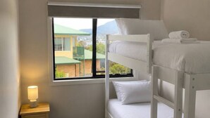 Een slaapkamer met stapelbed, raam, bedlamp en plafondventilator.