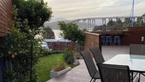 Een houten terras met een tafel en stoelen, met uitzicht op een waterpartij en een brug.