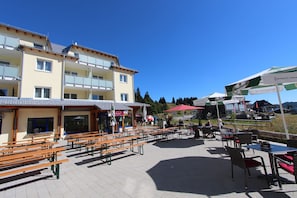 Een terras met houten banken en tafels, een gebouw met balkons en parasols.