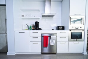 Una cocina moderna con armarios blancos, lavavajillas de acero inoxidable, cafetera y horno empotrado.