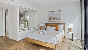 Een moderne slaapkamer met een groot bed, een spiegel, een lijst met een foto en een kleine tafel met lampen.