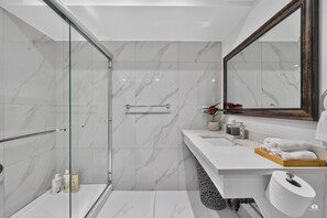 A modern bathroom with a glass shower enclosure, a white marble backsplash, and a large mirror.