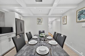 A modern kitchen with a dining area, featuring a stainless steel refrigerator, a flat-screen TV, and a marble countertop.