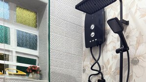 Brusebad med både håndbruser og fast monteret brusehoved, en glasdør og en bruseforhæng med blomstermønster.