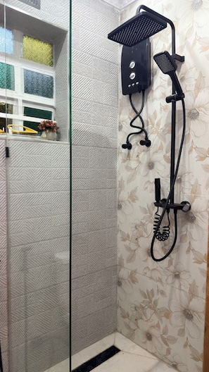 Une douche équipée d’un pommeau de douche à main et d’un pommeau fixé au mur, d’une porte en verre et d’un rideau de douche à motifs floraux.
