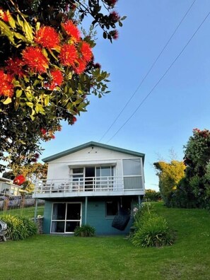 A two-story house with a balcony, a garage, and a well-maintained lawn. - Oakura Beachfront Bach + Close to Everything (Ōakura)