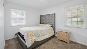Une chambre à coucher avec un lit, une commode et deux fenêtres équipées de stores.