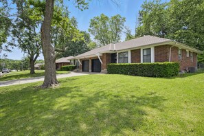 A single-story brick house with a front porch, a garage, and a well-maintained lawn. - Modern 3BR KC Getaway Minutes From Stadiums (Kansas City)