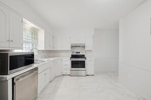 A kitchen with white cabinets, a stainless steel microwave, an oven, and a dishwasher. - Modern 3BR KC Getaway Minutes From Stadiums (Kansas City)