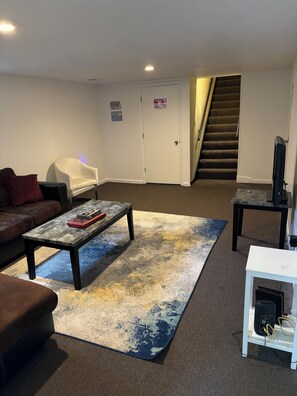 A living room with a sofa, a coffee table, a TV stand, and a staircase. - Modern 3BR KC Getaway Minutes From Stadiums (Kansas City)