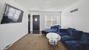 Un salon avec un canapé bleu, une table basse en verre et un téléviseur fixé au mur.