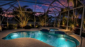 A swimming pool with a curved design, surrounded by palm trees and a glass enclosure. - Blue Pelican Stay - New listing with Hot Tub and Heated Pool (Port St. Lucie)