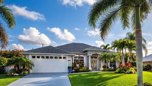 A two-story house with a garage, surrounded by well-maintained lawns and palm trees. - Blue Pelican Stay - New listing with Hot Tub and Heated Pool (Port St. Lucie)