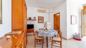 Un comedor con una mesa dispuesta para dos, sillas de madera, un armario, un televisor y un aire acondicionado instalado en la pared.