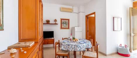 A dining area with a table set for two, wooden chairs, a cabinet, a television, and a wall-mounted air conditioner.