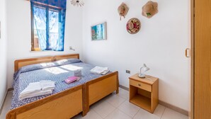 Un dormitorio ordenado con cama, mesita de noche y un pequeño escritorio con lámpara.