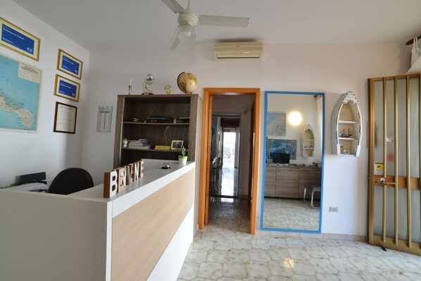 A reception desk with a nameplate, a ceiling fan, a map on the wall, and a door leading to a kitchen area. - Leuca Relax&Sea n.8d, Castrignano del Capo, Italy (Castrignano del Capo)