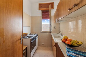 A compact kitchen with a stove, sink, and a window with blinds. - Leuca Relax&Sea n.8d, Castrignano del Capo, Italy (Castrignano del Capo)