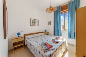 A bedroom with a bed, a nightstand, a lamp, a window with curtains, and a door. - Leuca Relax&Sea n.8d, Castrignano del Capo, Italy (Castrignano del Capo)
