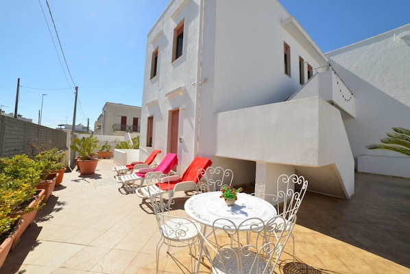 A white building with a patio area featuring a round table, white metal chairs, and potted plants. - Leuca Relax&Sea n.8d, Castrignano del Capo, Italy (Castrignano del Capo)