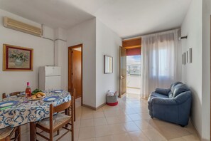 A dining area with a table set for two, a blue sofa, and a door leading to a balcony. - Leuca Relax&Sea n.8d, Castrignano del Capo, Italy (Castrignano del Capo)