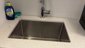 Een keuken met een spoelbak van roestvrij staal, witte keukenkastjes en een aanrecht.