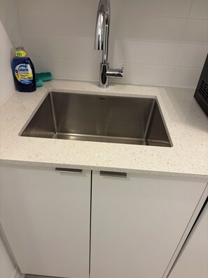 A kitchen with a stainless steel sink, white cabinets, and a countertop.
