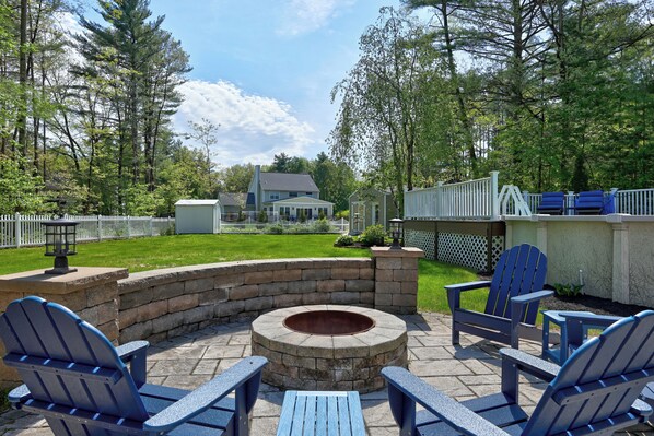 A backyard with a stone fire pit, Adirondack chairs, and a white fence. - Modern Oasis-Pool, Hot-tub, Bar near Saratoga (Ballston Spa)