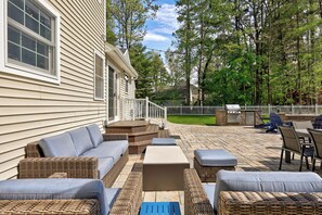 A patio with outdoor furniture, a grill, and a white fence.