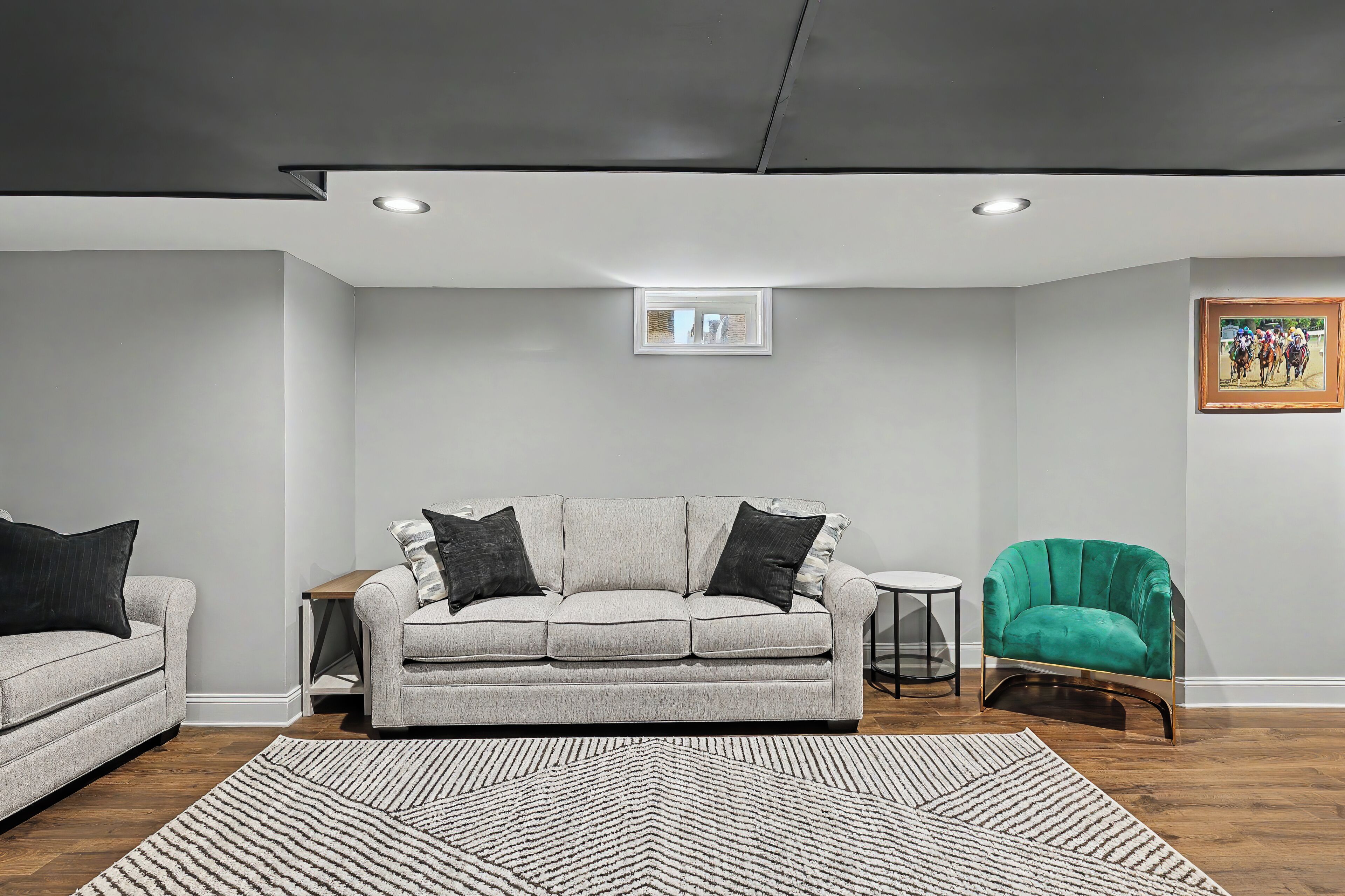 Ein modernes Wohnzimmer mit grauem Sofa, einem grünen Sessel, einem gemusterten Teppich und einem gerahmten Bild an der Wand.
