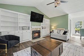 Un salon avec une cheminée, un canapé, un téléviseur et un ventilateur de plafond.