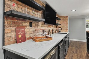 Een keuken met een bakstenen muur, een flatscreen televisie, een bord met wijn erop en een dienblad met glazen.