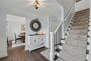 A staircase with a textured carpet, a dining area with a white cabinet and a mirror, and a ceiling light fixture.