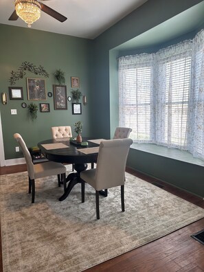 A dining room with a table, chairs, a chandelier, framed pictures, and a window with curtains. - Verbena Executive Cottage (Morris)